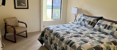 A bedroom with a bed, a chair, a window, and a picture on the wall.