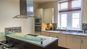 A modern kitchen with a central island, built-in oven, microwave, and a window with blinds. - Luxury Apartment No.1, Whitefield (Whitefield)