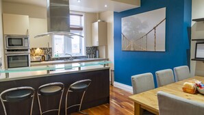 A modern kitchen with a glass island, stainless steel appliances, and a blue accent wall. - Luxury Apartment No.1, Whitefield (Whitefield)