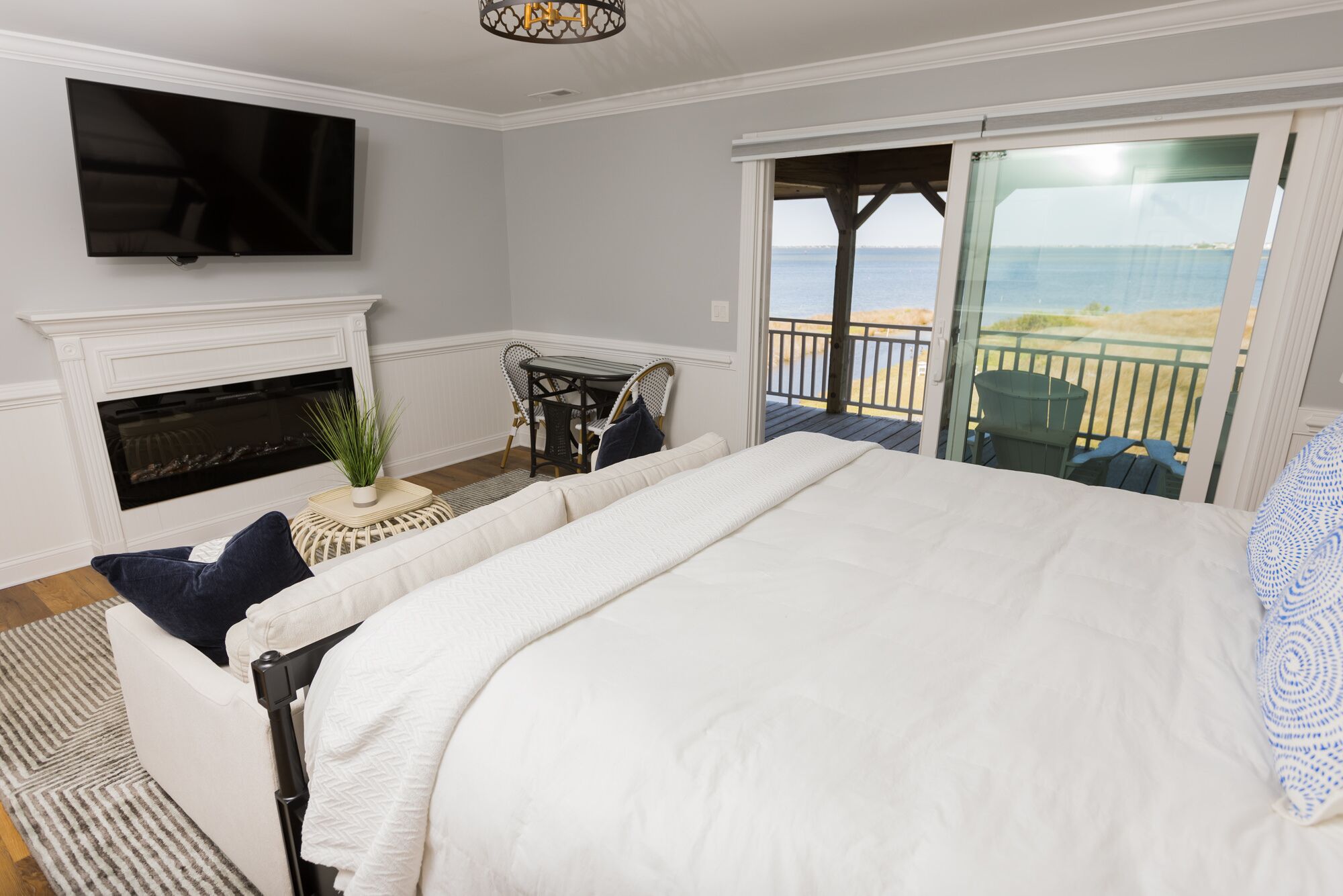 Een slaapkamer met een groot bed, een open haard, een televisie en een balkon met uitzicht op het strand.