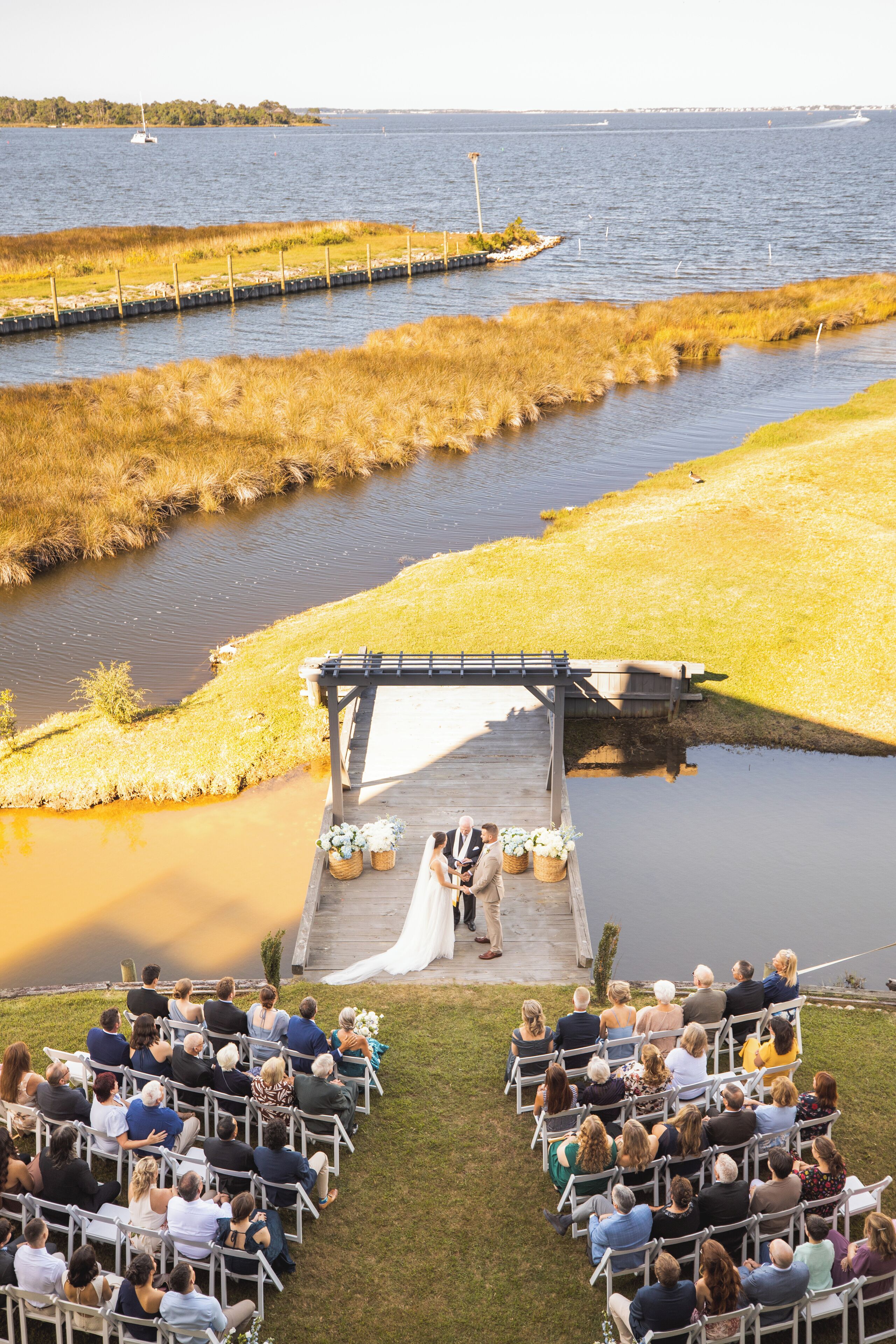 A wedding ceremony by a lake with a wooden platform and chairs arranged for guests.