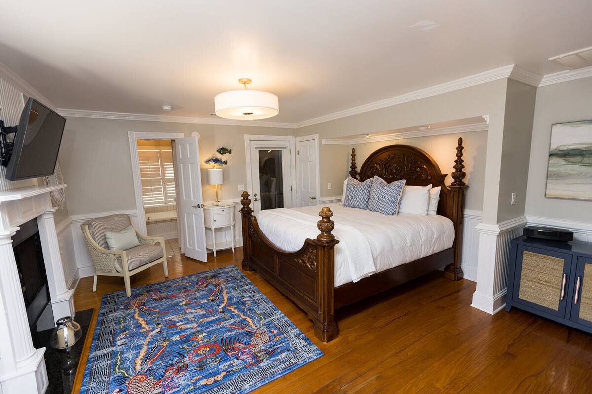 A bedroom with a large bed, a television, a fireplace, and a rug.