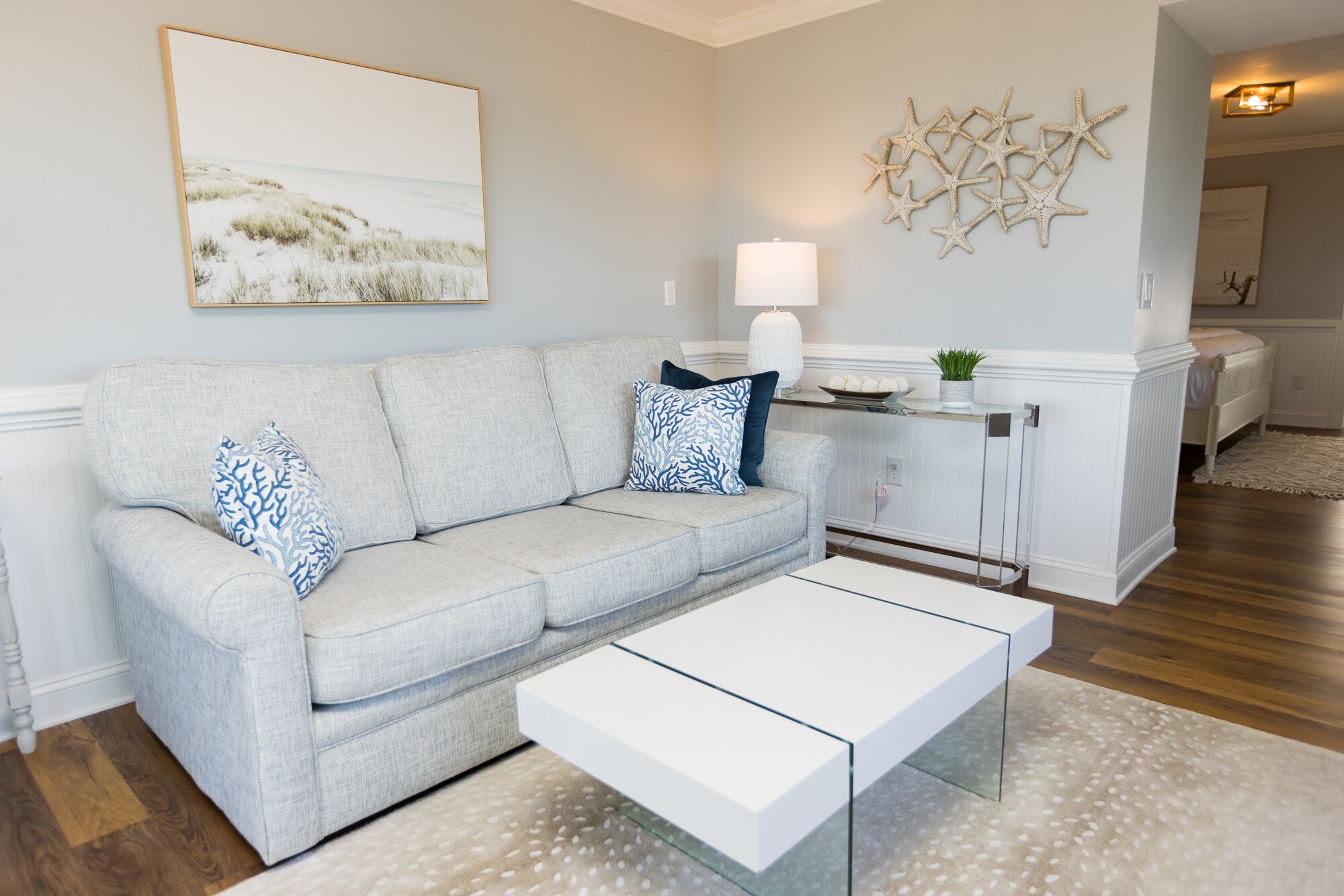 A living room with a grey sofa, a white coffee table, and a painting of a beach scene.