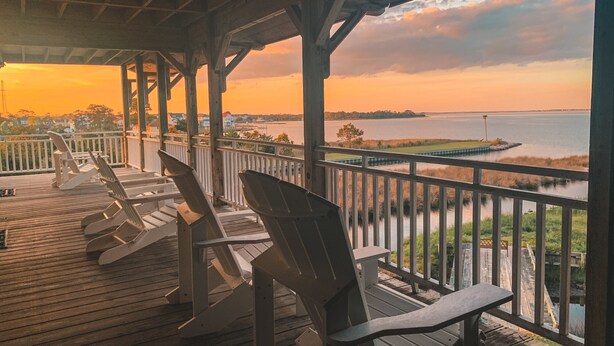 A wooden deck with Adirondack chairs overlooking a body of water at sunset. - The Burrus House Inn Waterfront Suites (Manteo)