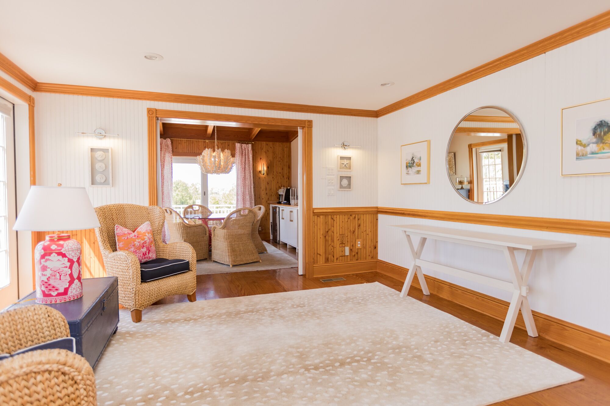 Un salon chaleureux avec des meubles en osier, une console blanche et un grand miroir.