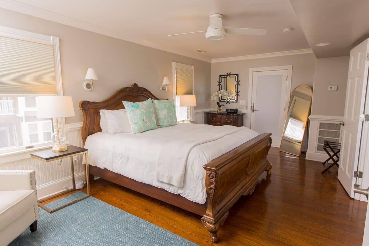 A spacious bedroom with a large wooden bed, a ceiling fan, and a view of the city through the window.