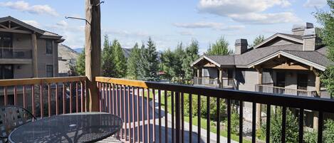 A wooden deck with a metal table and chairs, overlooking a residential area with houses and trees.