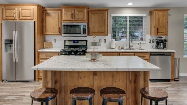 Una cocina moderna con armarios de madera, electrodomésticos de acero inoxidable, una isla de mármol con taburetes y una ventana con vistas al exterior.
