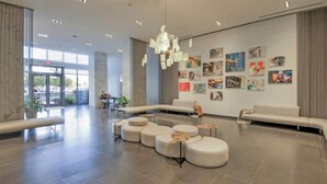 Eine geräumige Lobby im modernen Stil mit einer Sitzecke, Sofas, Poufs, einer Wand mit Kunstwerken und einem großen Fenster, das für natürliches Licht sorgt.