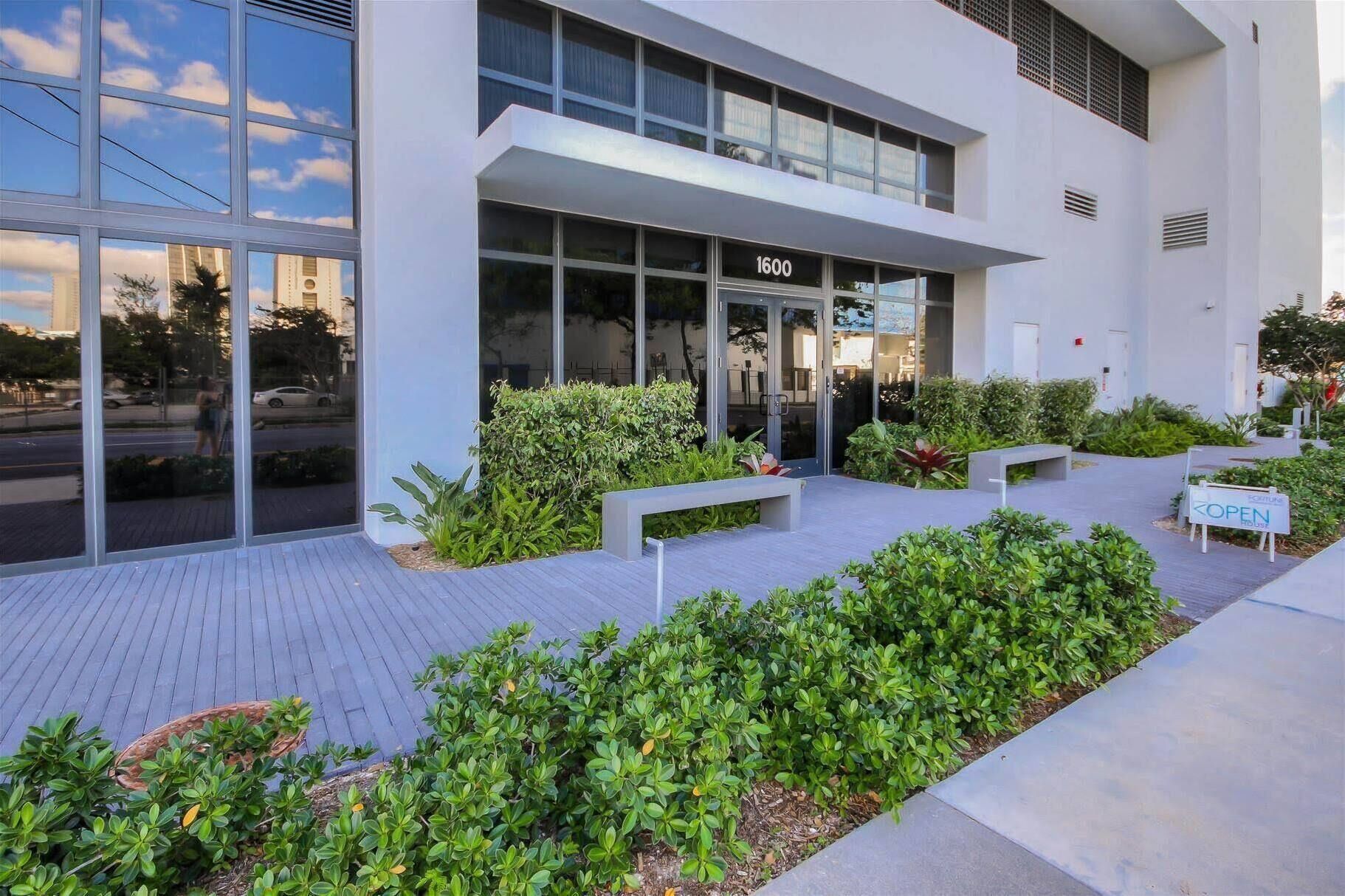 A modern building with large glass windows, a number '1600' sign, and a landscaped outdoor area with benches and plants.