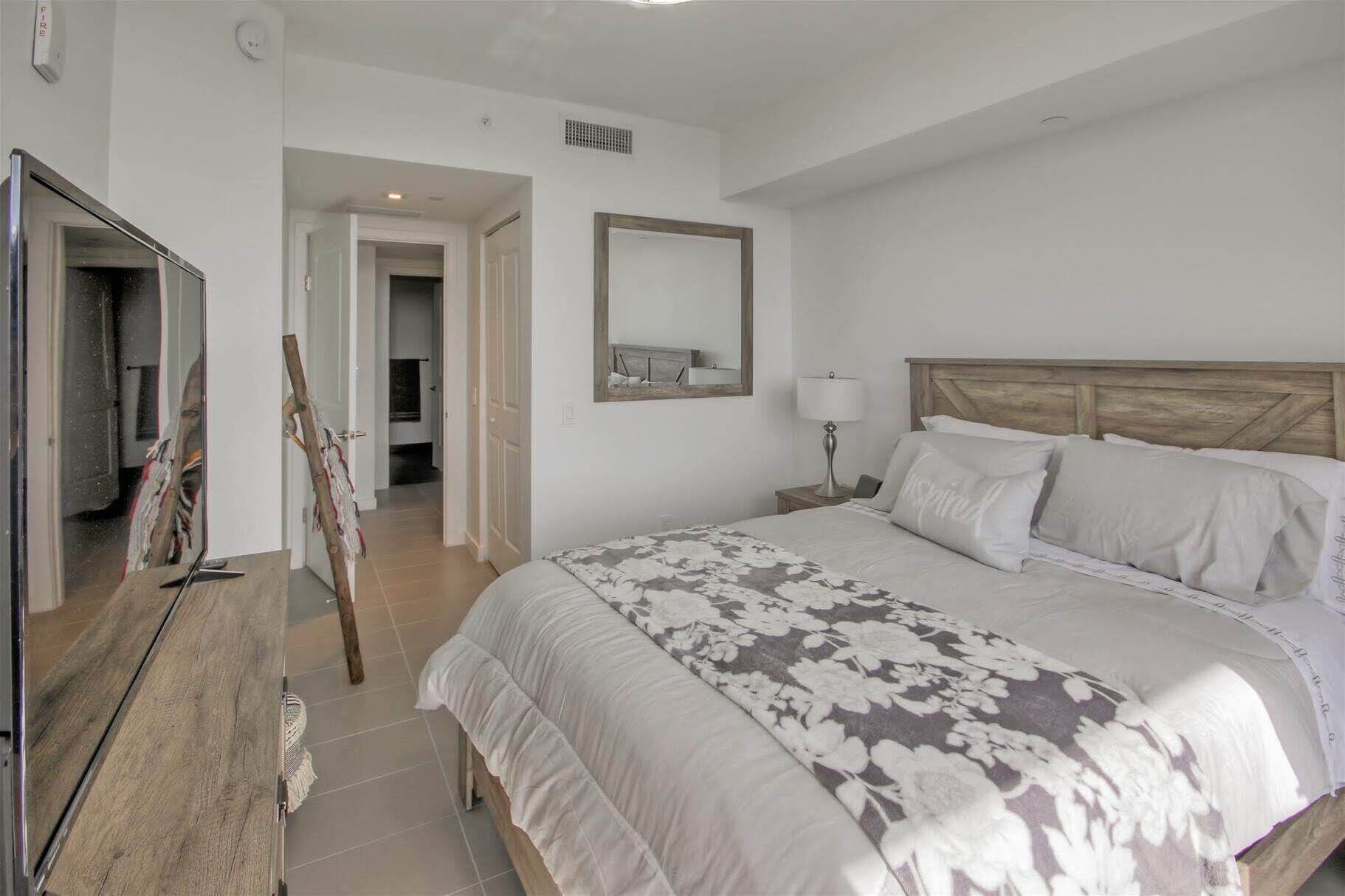 Un dormitorio con una cama grande, cabecera de madera, lámpara de noche y un espejo en la pared.