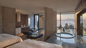 A modern hotel room with two beds, a seating area, a hot tub, and a balcony with a city view.