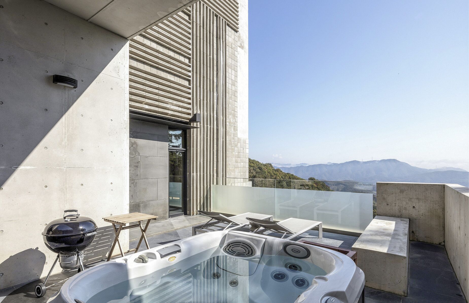 Un patio exterior moderno con un jacuzzi, una parrilla y vistas a las montañas.