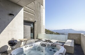 A modern outdoor patio with a hot tub, a grill, and a view of mountains. - Memory Maker (Gapyeong)