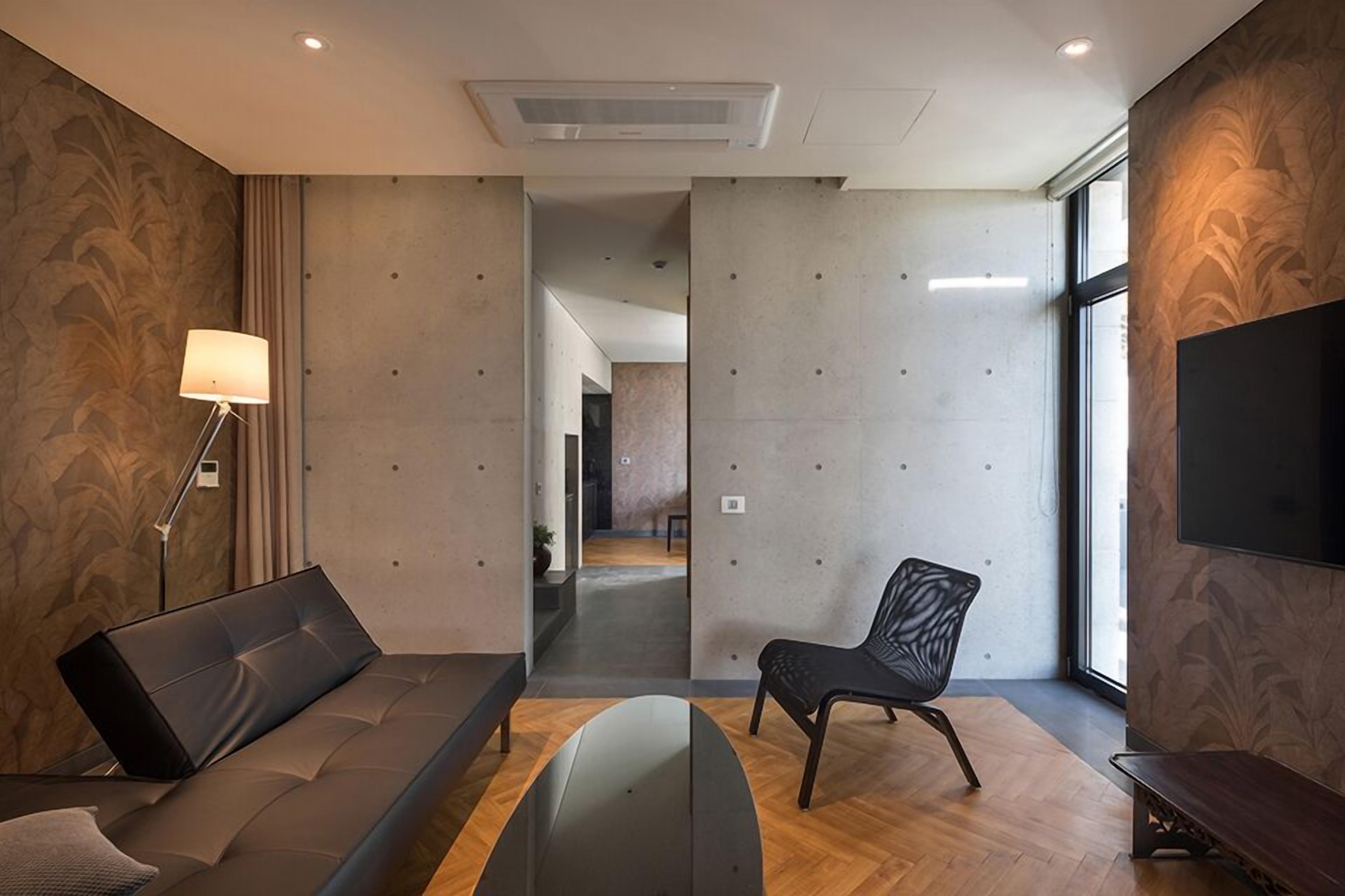 A modern hotel room with a sofa, a chair, a lamp, and a TV.