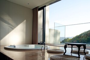 A modern bathroom with a large bathtub, a glass-enclosed shower area, and a view of a mountainous landscape. - Memory Maker (Gapyeong)