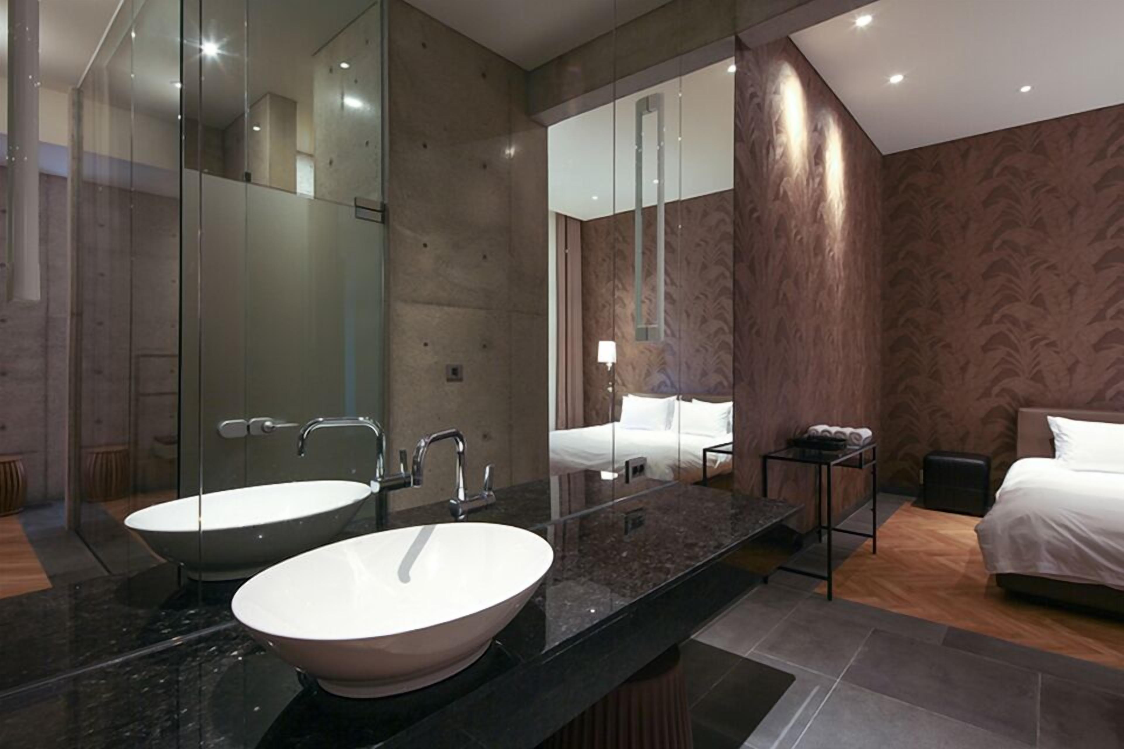 Ein modernes Badezimmer mit zwei Waschbecken, einem großen Spiegel und einem Bett im angrenzenden Raum.