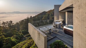 A modern outdoor terrace with a hot tub, seating area, and a view of a forested mountain range.