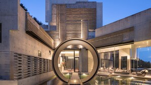 A modern building with a circular glass structure in the center, a pool, and outdoor seating.
