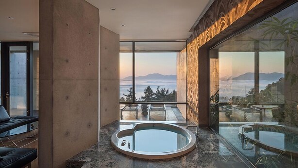 A modern bathroom with a large bathtub, a glass-enclosed shower area, and a view of mountains through large windows.