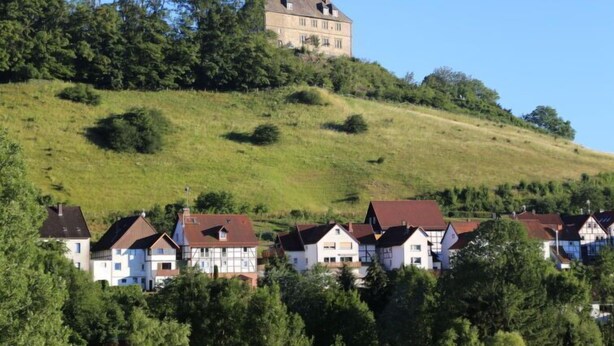 A hilltop house with a traditional design, surrounded by a residential area with houses.