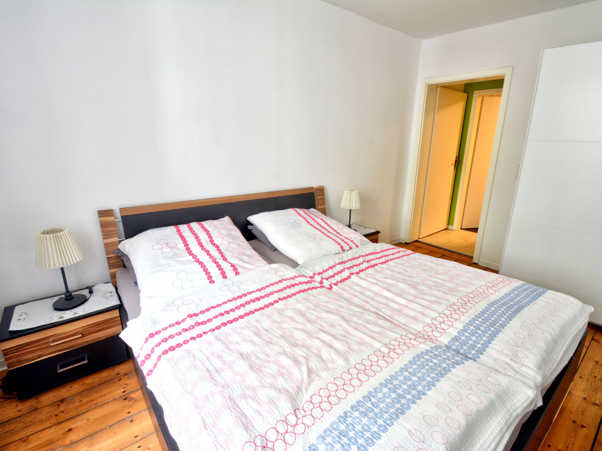 Un lit bien fait, recouvert d’une couvre-lit à motifs, une table de chevet avec une lampe et un plancher en bois.