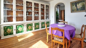 A dining area with a wooden table and chairs, a white cabinet with glass doors, and a painting on the wall.