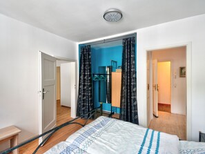 Une chambre à coucher avec un lit, un plancher en bois, un luminaire au plafond et une porte donnant sur une autre pièce.