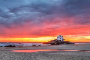A coastal scene with a white building on a rock, surrounded by ocean waves and a sunset sky. - House in Beach- Oporto (Arcozelo)