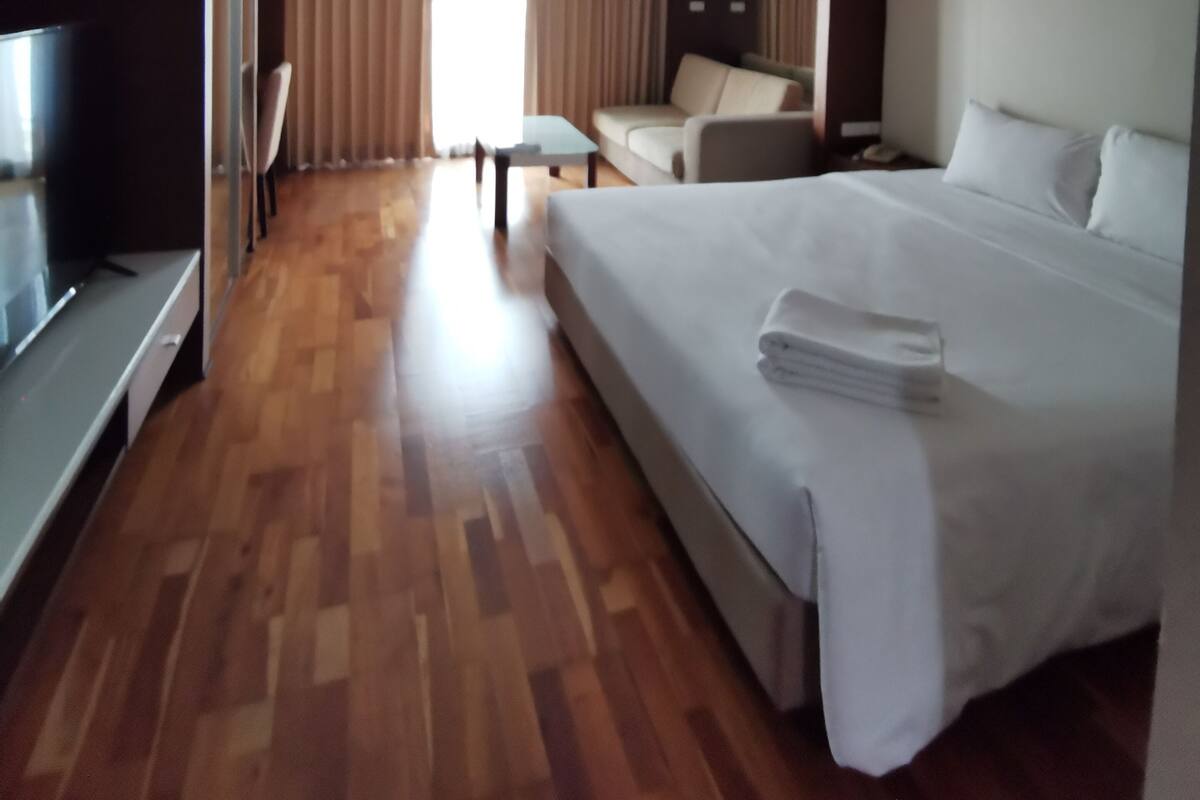 Hotellihuone, jossa on suuri sänky, televisio, sohva ja ruokapöytä.