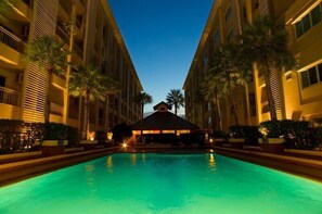 A hotel pool area with a central gazebo, surrounded by multi-story buildings with balconies and palm trees. - The Ninth Place Serviced Residence (Bangkok)