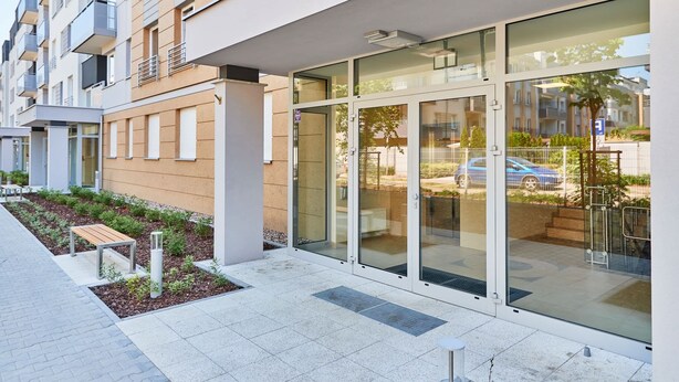 A modern building with large glass doors, a bench, and a small garden area.