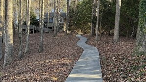 Ein Betonweg durch ein bewaldetes Gebiet, im Hintergrund eine Holzhütte.