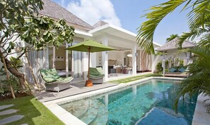 A modern pool area with a clear pool, lounge chairs, and a covered seating area.
