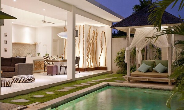 A modern outdoor living area with a pool, a dining area, and a seating area with a canopy.