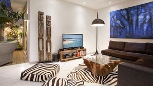 A modern living room with a flat-screen TV, a large abstract painting, and a wooden coffee table. - Le Chloe Villas (Seminyak)