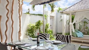 A glass table set for dining outdoors with a white canopy and striped cushions. - Le Chloe Villas (Seminyak)