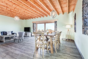 A spacious living area with a wooden ceiling, a dining table with chairs, a sofa, and a TV. - Stunning Villa "Tranquila" with Sea View, Mountain View, Pool, Garden & Terrace (La oliva, Fuerteventura)