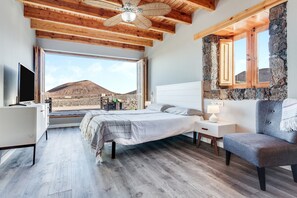 A bedroom with a bed, a desk, a chair, a TV, and a large window with a mountain view. - Stunning Villa "Tranquila" with Sea View, Mountain View, Pool, Garden & Terrace (La oliva, Fuerteventura)
