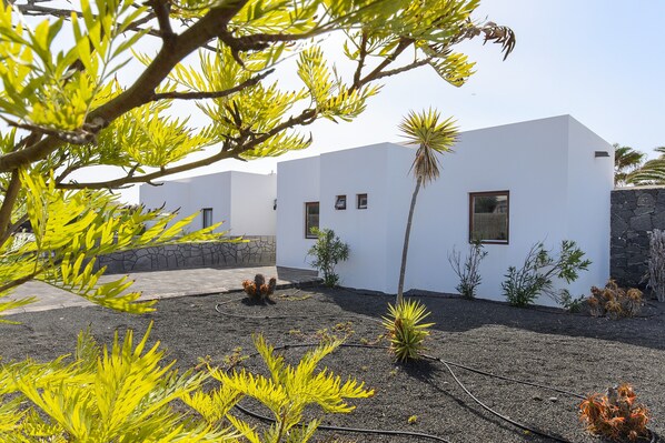 A modern building with white walls, small windows, and a stone wall. - Beautiful Villa "Mariola" Close to Beach with Heated Pool, Terrace, Garden & Wi-Fi (Playa blanca)
