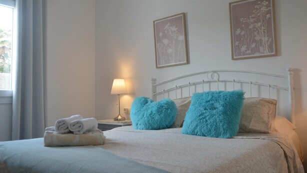 A neatly made bed with rolled towels, two heart-shaped pillows, a bedside lamp, and two framed floral artworks on the wall. - Beautiful Villa "Mariola" Close to Beach with Heated Pool, Terrace, Garden & Wi-Fi (Playa blanca)