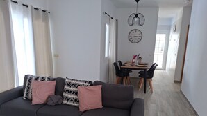 Ein modernes Wohnzimmer mit einem dunkelgrauen Ecksofa, einem Glastisch und einem Essbereich mit Holztisch und schwarzen Stühlen.