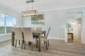 Een eetgedeelte met een houten tafel en stoelen, een hanglamp en een schilderij aan de muur.