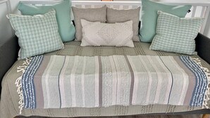 A bed with a striped blanket, multiple pillows, and a hanging light fixture above. - Oceanfront, Blissful Sunrises, Beach Gear, BBQ (St. Augustine)