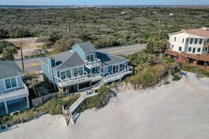 Ein Strandgrundstück mit einem großen Haus, mehreren Balkonen, einer überdachten Terrasse und einem Strandabschnitt mit Sand.