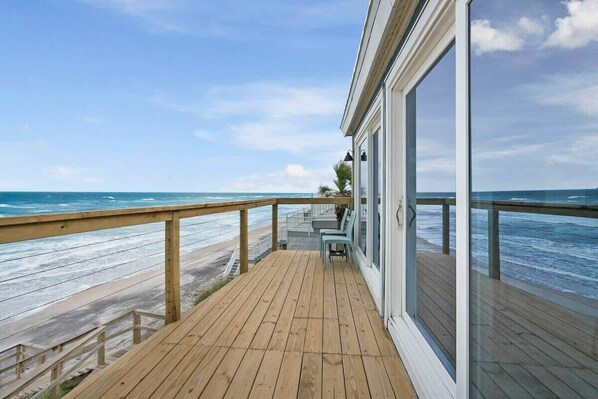 Una terraza de madera con un portón de vidrio que da a un balcón con vistas al océano.