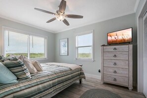 A bedroom with a bed, a ceiling fan, a dresser, and a television on a stand.