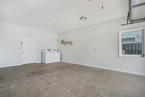 A room with a door, a washing machine, a shelf with cleaning supplies, and a window.