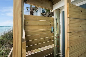 A wooden beach house with a sliding door, a small shelf with a bottle, and a view of the ocean.