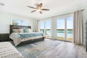 Een slaapkamer met een groot bed, een plafondventilator en uitzicht op de oceaan door grote schuifdeuren.
